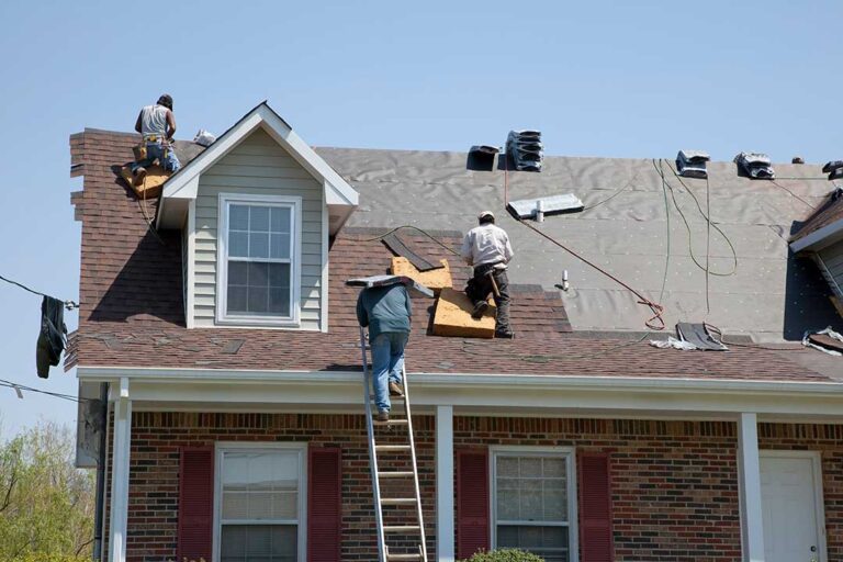 Close view of curled and cracked asphalt shingles on a weathered residential roof with gutters below.