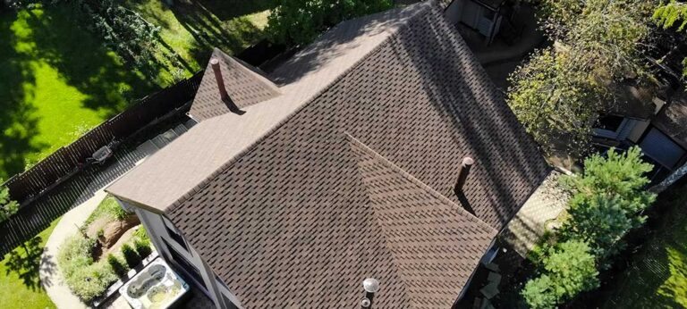 A residential home with a sloped roof beside a modern flat-roof addition after light snowfall.